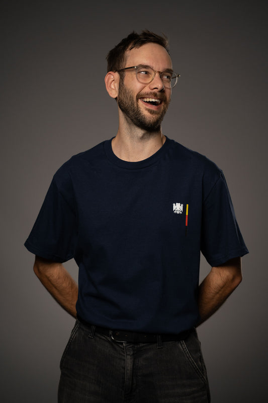 Dunkelblaues T-Shirt mit kleinem Bundesfrosch-Logo auf der linken Brust. Das Logo zeigt einen stilisierten Frosch mit Flügeln in Weiß, daneben ein vertikaler Streifen in Schwarz, Rot und Gelb.