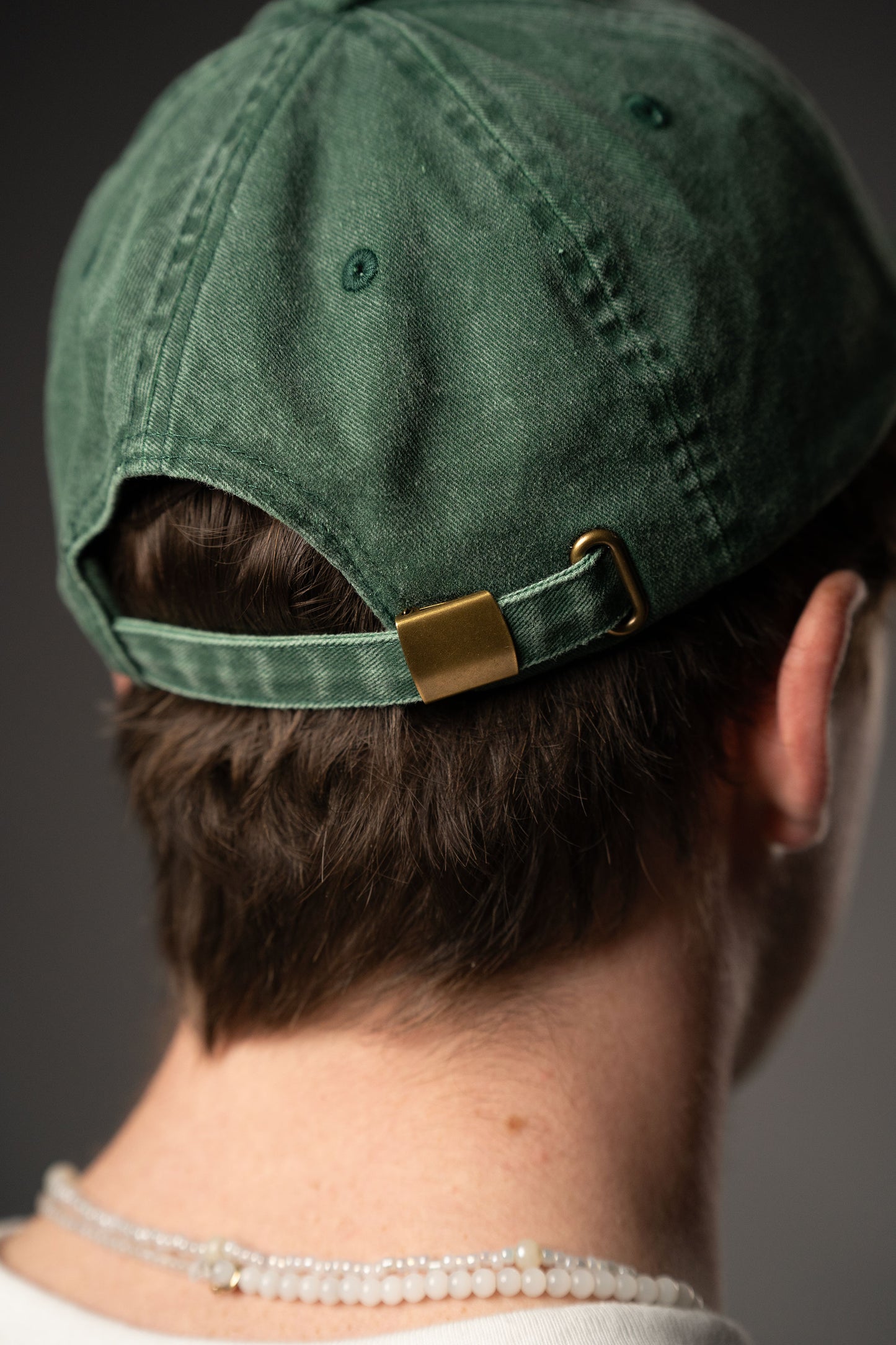 Nahaufnahme der Rückseite einer grünen Cap aus Baumwollstoff mit verstellbarem Riemen und messingfarbenem Metallschieber.