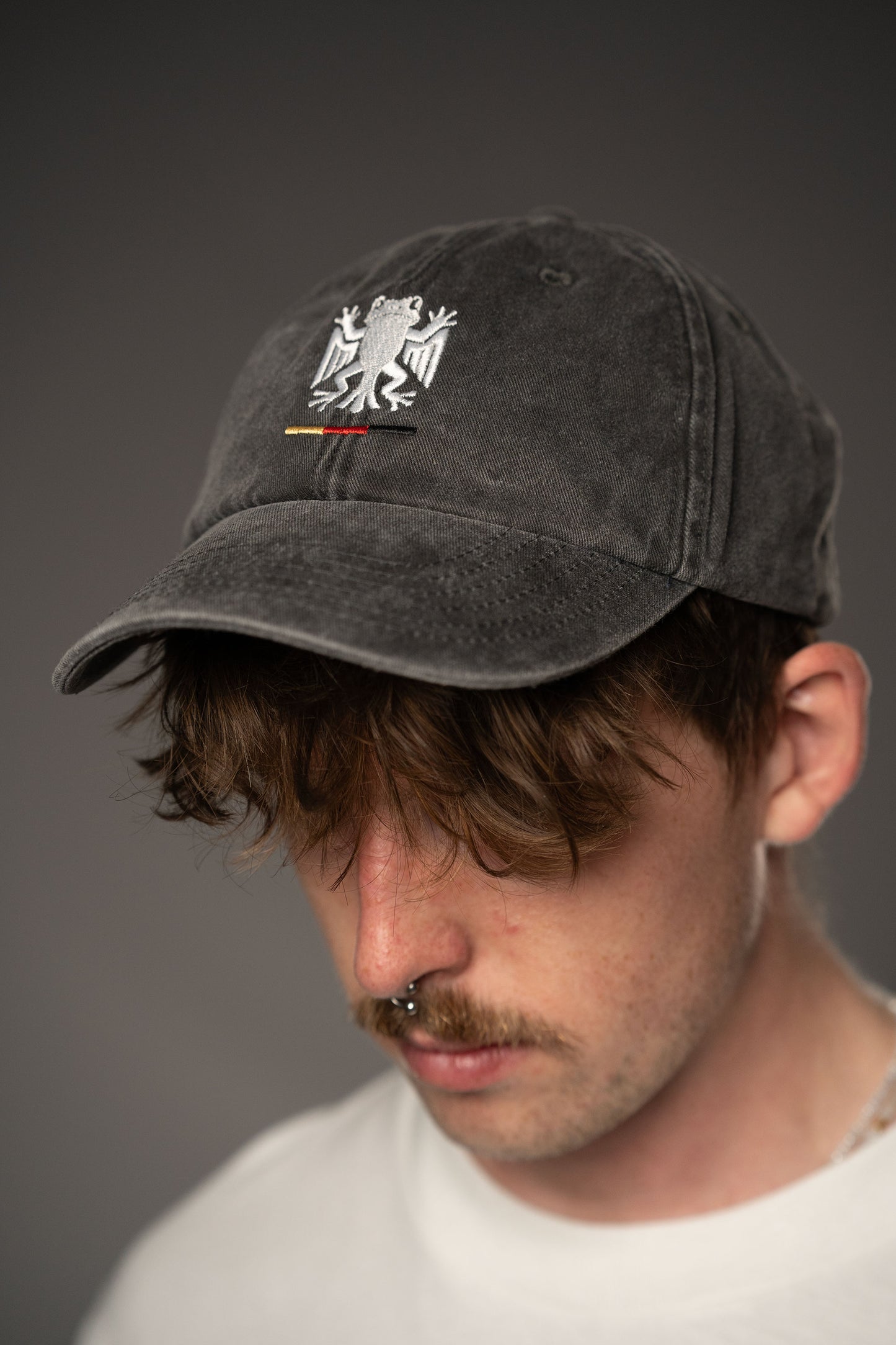 Schwarze Cap mit Bundesfrosch-Stick auf der Vorderseite, getragen von einer Person in weißem T-Shirt. Die Cap hat eine gewaschene Struktur und zeigt auf der Vorderseite das weiße Froschsymbol mit Streifen in Schwarz-Rot-Gold.