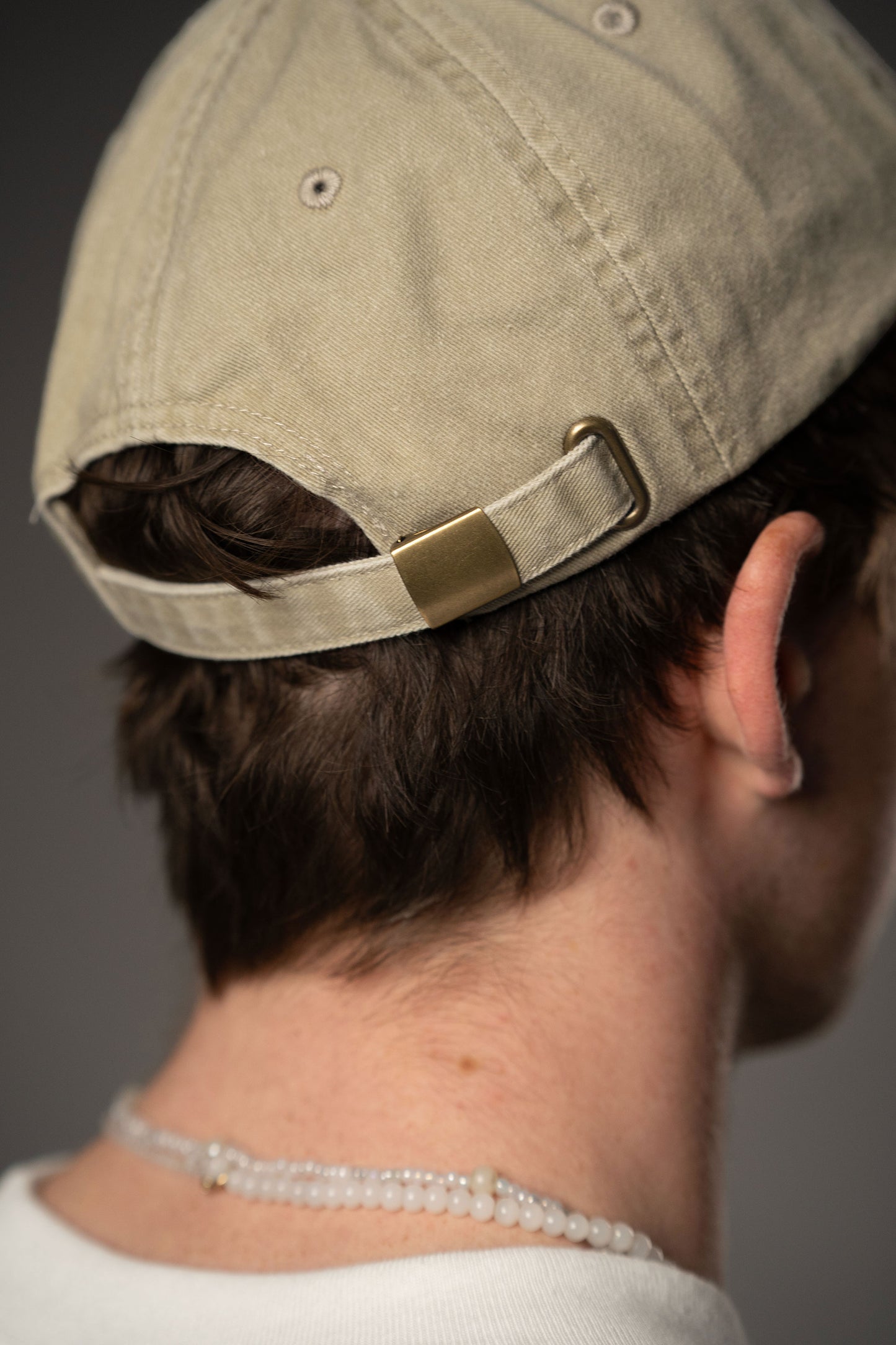 Rückansicht der beigefarbenen Baseballcap mit verstellbarem Riemen und Metallschnalle in Messingoptik.