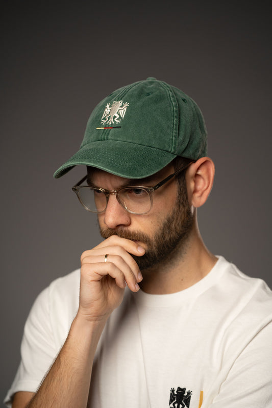 Seitliche Ansicht einer grünen Cap mit weiß gesticktem Bundesfrosch-Logo und kleiner Stickerei in Schwarz, Rot und Gelb. Die Cap wird zu einem weißen T-Shirt getragen.