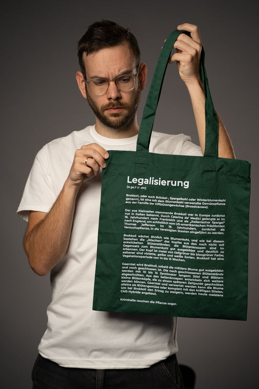 Dunkelgrüne Stofftragetasche mit weißem Aufdruck „Legalisierung“ und humorvollem Text über Brokkoli, gehalten von einer Person im weißen T-Shirt.