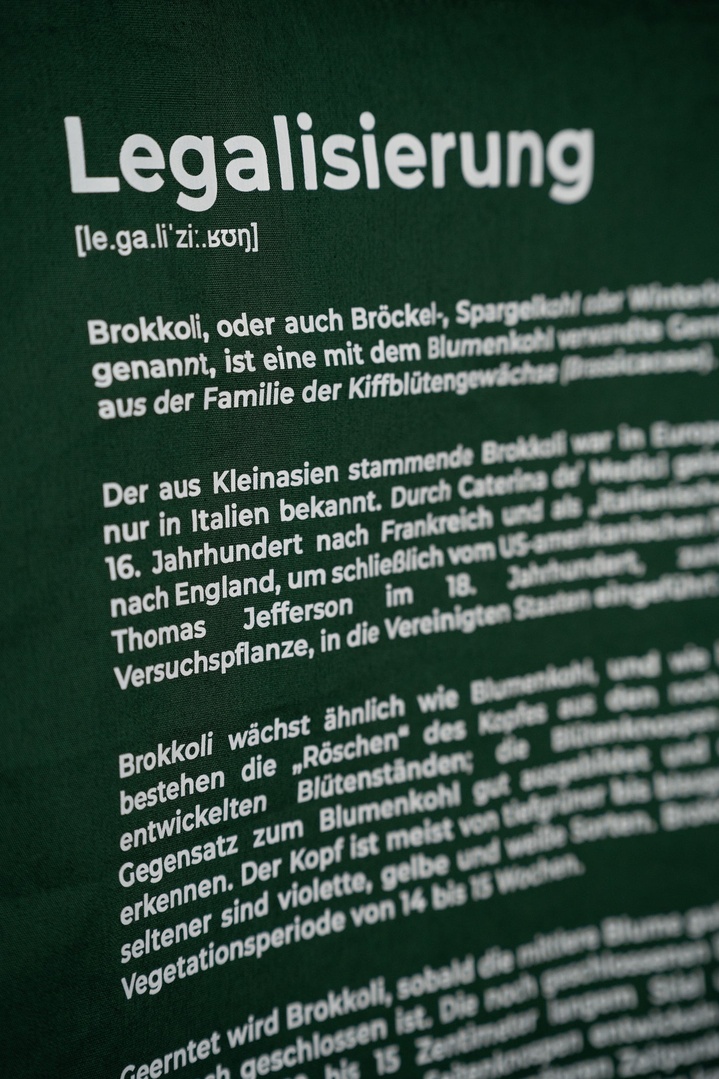 Nahaufnahme der dunkelgrünen Stofftasche mit weißem Aufdruck „Legalisierung“ und detailliertem Text über Brokkoli.