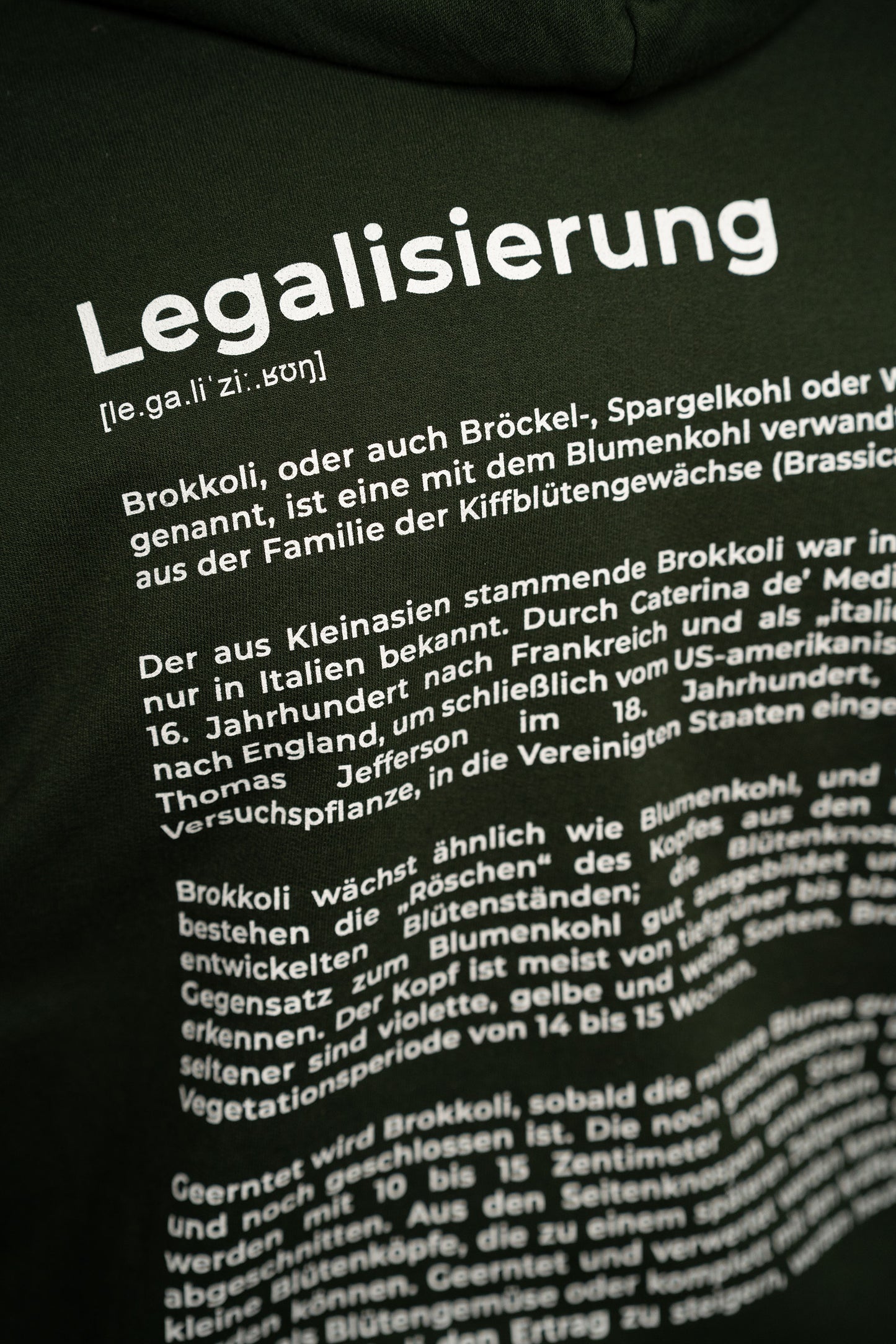 Detailaufnahme des Rückendrucks auf dem dunkelgrünen Hoodie. Der weiße Text zeigt den Titel „Legalisierung“ und darunter einen erklärenden Absatz über Brokkoli als Gemüseart, in humorvollem Lexikonstil gestaltet.