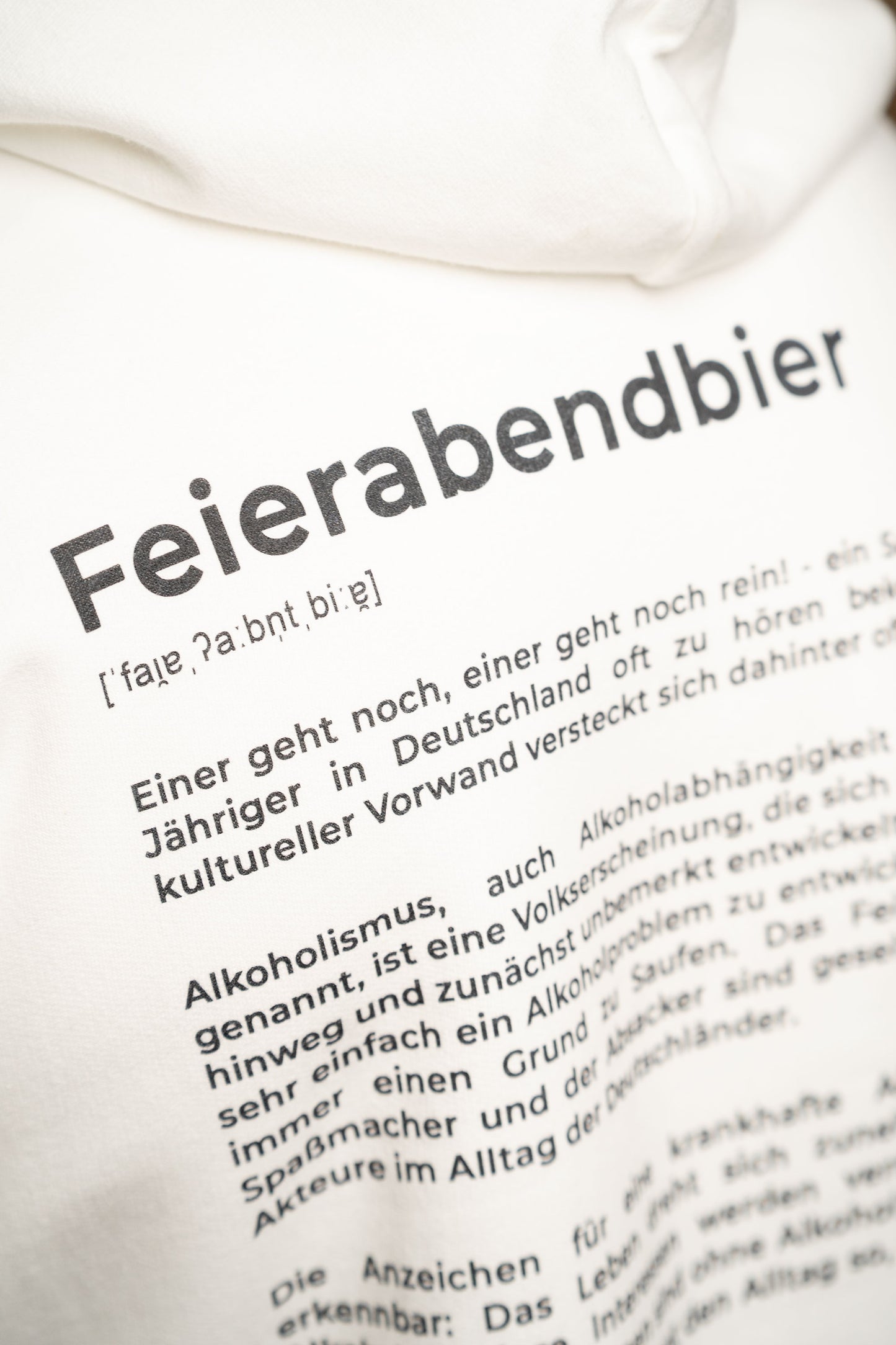 Detailaufnahme des Rückendrucks auf dem weißen Hoodie mit dem Schriftzug „Feierabendbier“ und einer ausführlichen textbasierten Definition darunter.