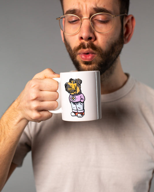 Weiße Keramiktasse mit farbigem Aufdruck auf der Vorderseite. Das Motiv zeigt einen gezeichneten Hund mit schwarzem Kopf und braunem Fell, der aufrecht steht und Kleidung trägt: eine lila Kapuzenjacke mit Blümchen-Print, hellblaue Hose und rote Schuhe. Die Illustration ist humorvoll und comicartig gestaltet. Die Tasse wird von einer Person in neutralem T-Shirt in der Hand gehalten – der Fokus liegt klar auf dem Design der Tasse.
