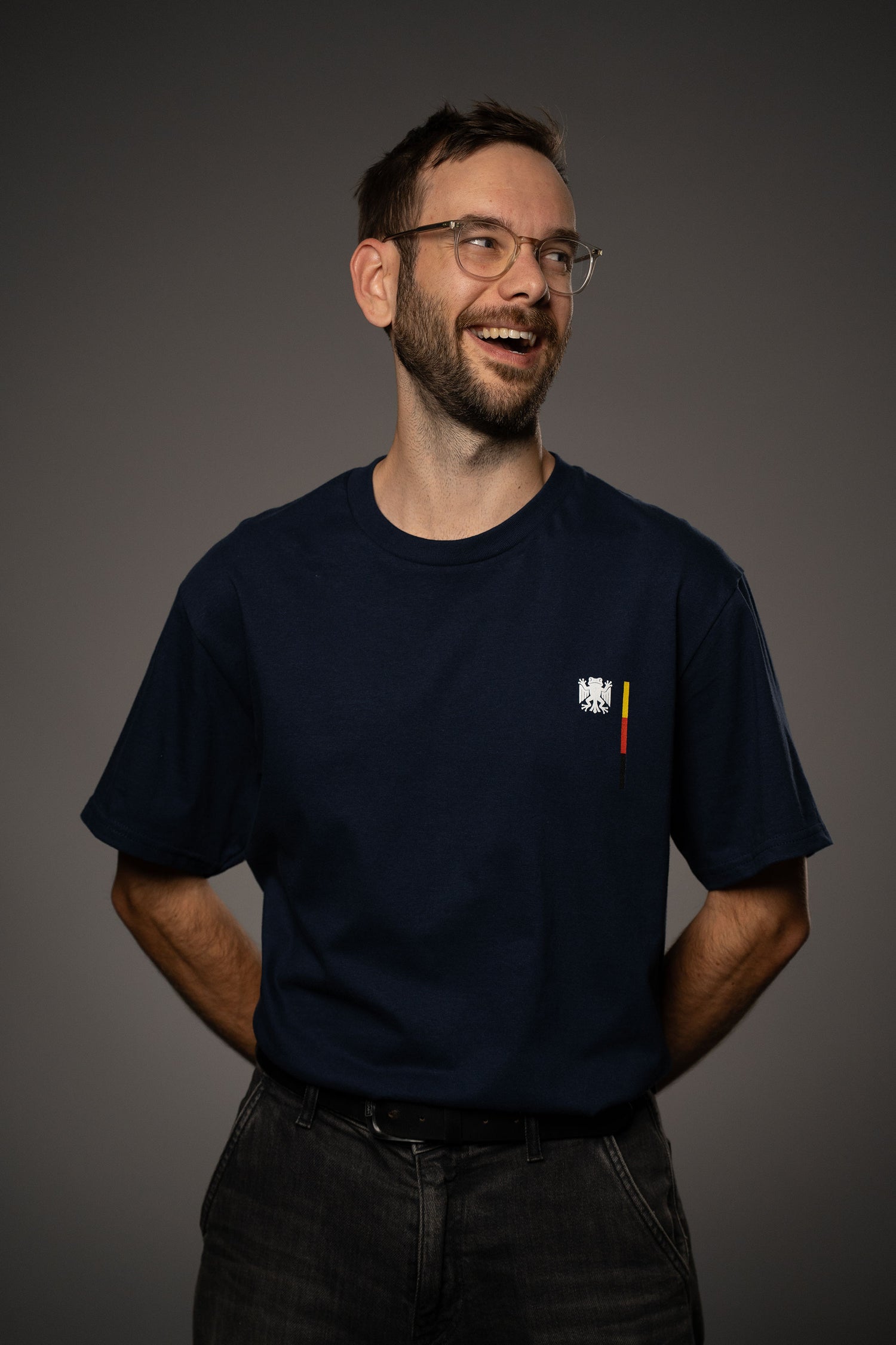 Dunkelblaues T-Shirt mit kleinem Bundesfrosch-Logo auf der linken Brust. Das Logo zeigt einen stilisierten Frosch mit Flügeln in Weiß, daneben ein vertikaler Streifen in Schwarz, Rot und Gelb.