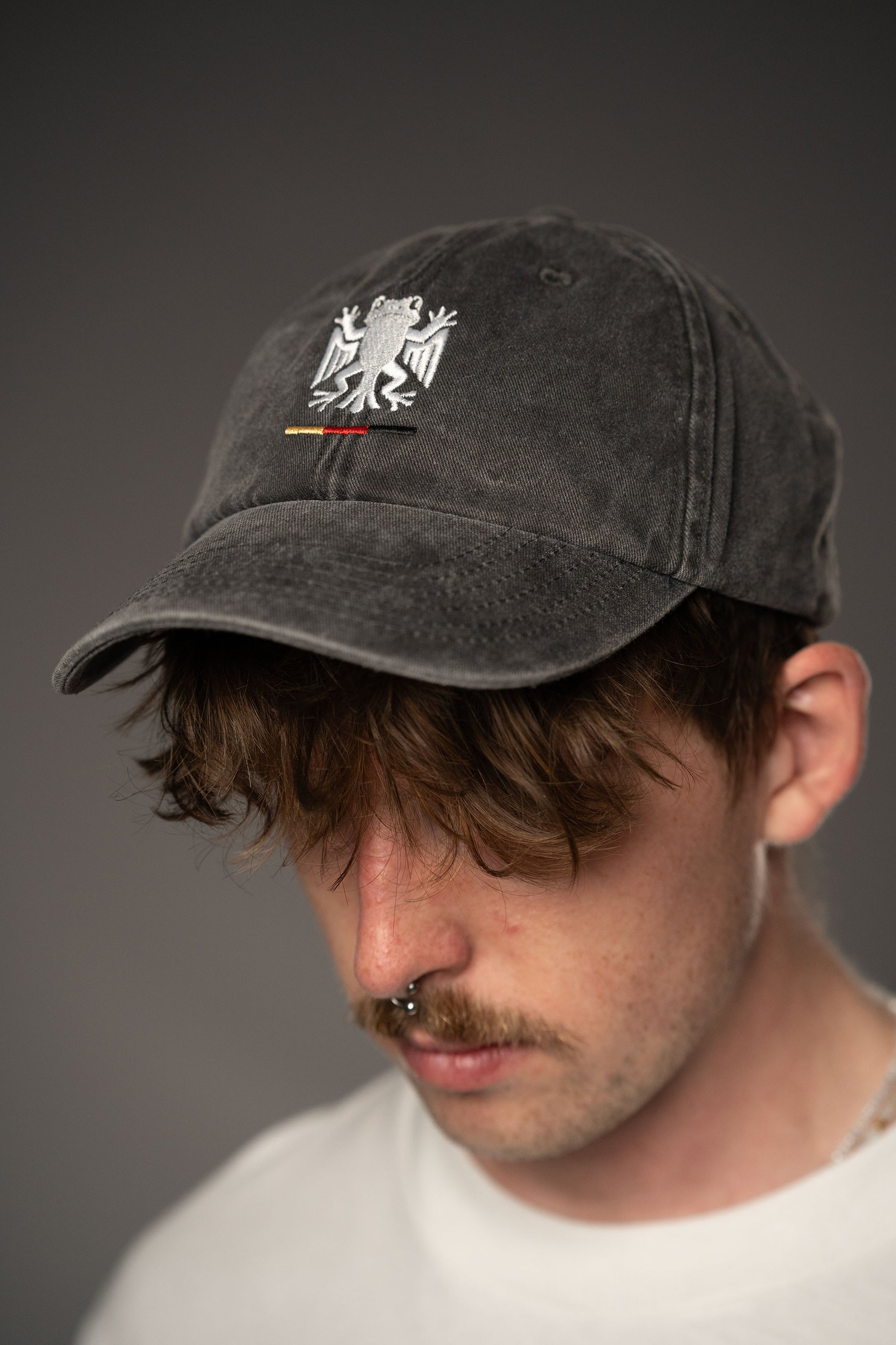 Schwarze Cap mit Bundesfrosch-Stick auf der Vorderseite, getragen von einer Person in weißem T-Shirt. Die Cap hat eine gewaschene Struktur und zeigt auf der Vorderseite das weiße Froschsymbol mit Streifen in Schwarz-Rot-Gold.