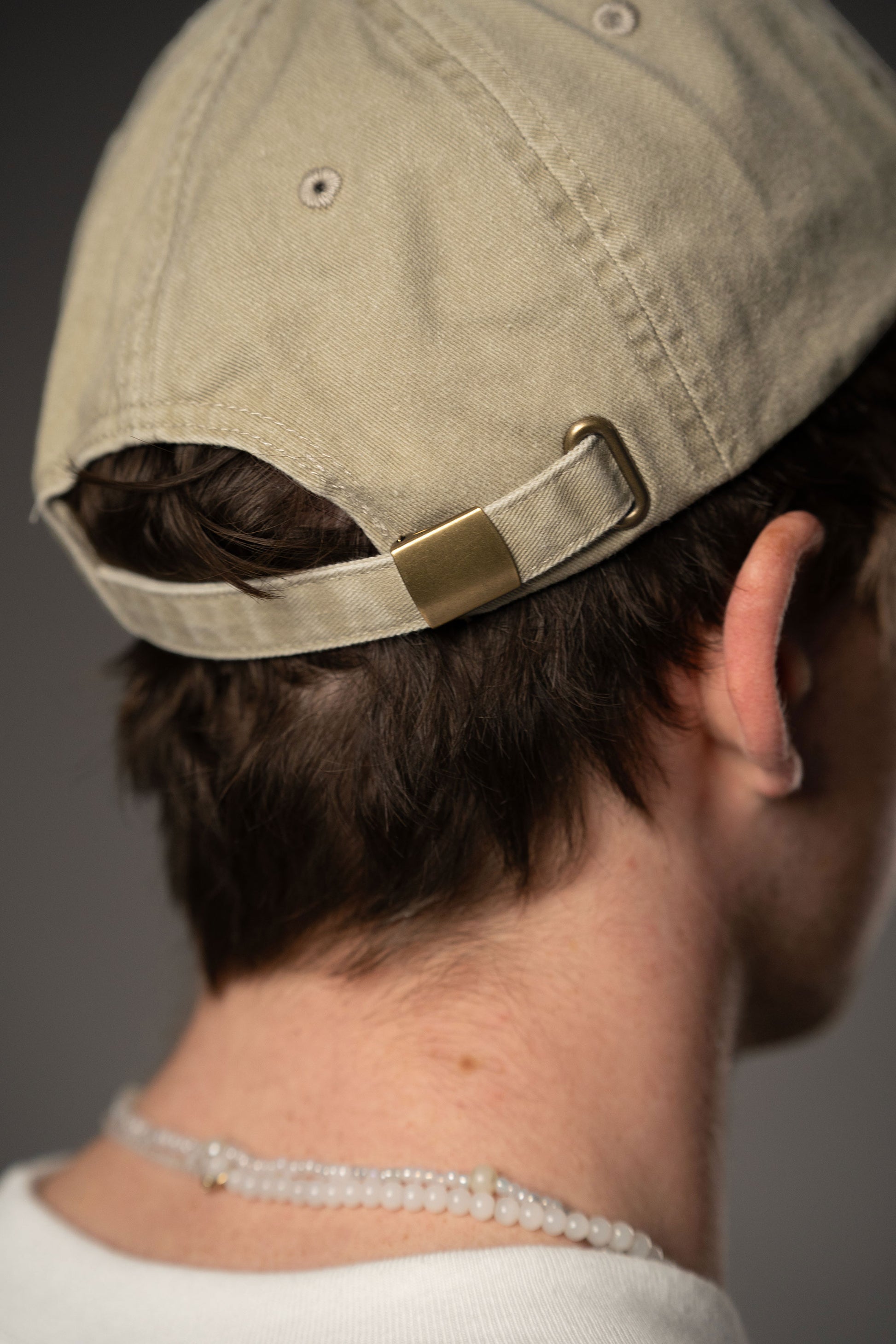 Rückansicht der beigefarbenen Baseballcap mit verstellbarem Riemen und Metallschnalle in Messingoptik.