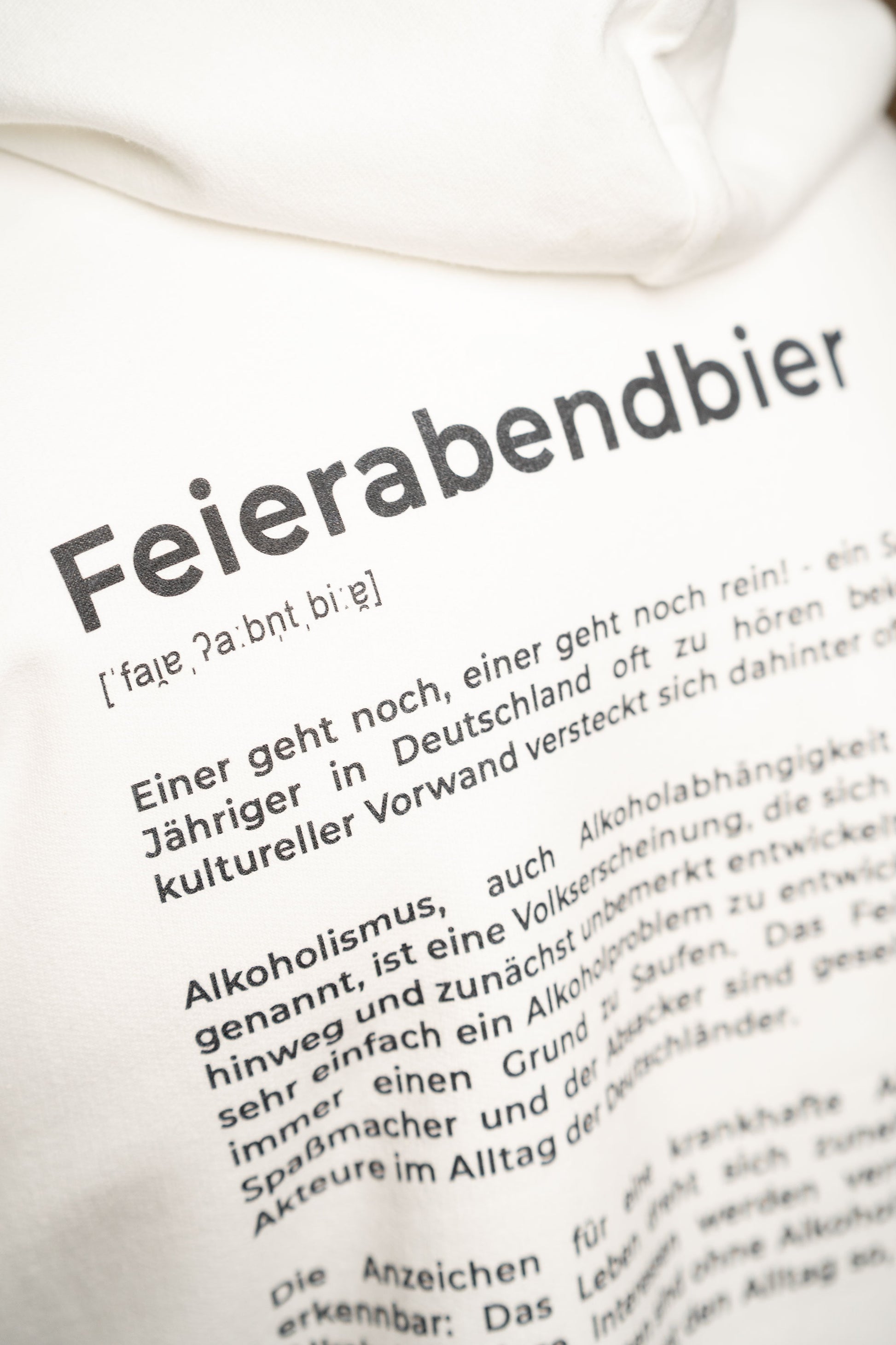 Detailaufnahme des Rückendrucks auf dem weißen Hoodie mit dem Schriftzug „Feierabendbier“ und einer ausführlichen textbasierten Definition darunter.
